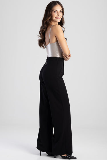 woman in a silver satin sleeveless top and black high-waisted wide-leg jumpsuit pants, standing in profile and smiling.