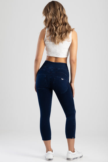woman seen from behind wearing a white lace crop top and dark blue capri jeans with back pockets and white sneakers