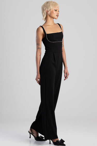 woman wearing a black sleeveless jumpsuit with thin straps and a sparkling chain detail at the bust, wide leg pants, black