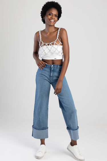 woman in a studio wearing light blue wide leg jeans with cuffs, white sneakers, and a white beaded lattice top