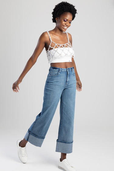 woman in light blue wide leg jeans with turned up cuffs, white sneakers, and a white crochet top