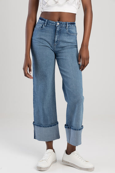 blue wide leg jeans with rolled cuffs worn by a model, paired with white sneakers and a white cropped top