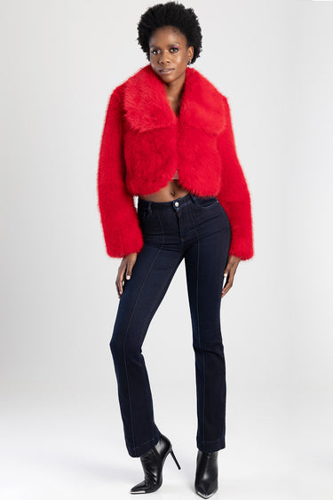 woman wearing red faux fur cropped jacket and dark blue bootleg jeans with contrast stitching, paired with black heeled