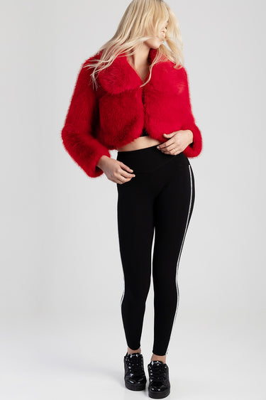 woman in a bright red faux fur jacket paired with black knit jeans with white side stripes and black sneakers