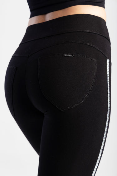 close up of black denim jeans on a model, back pocket with small metal tag and a silver rhinestone stripe along the side by