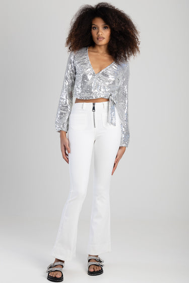 woman wearing white flare jeans with front zipper and pockets, paired with a silver sequin wrap top