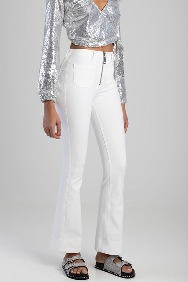 woman wearing white high waist flare jeans with a front zip, paired with a silver sequin top and silver sandals