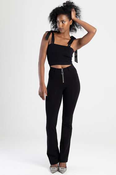 woman wearing black knit denim jeans with a front zipper and a cropped black top with tied shoulder straps