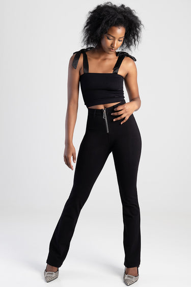 model wearing black high waisted jeans with front zipper, paired with a black cropped top with tied shoulder straps
