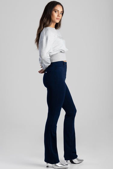 woman in a light grey knit sweatshirt and dark blue bootcut jeans, side profile.
