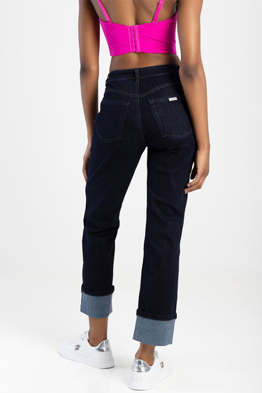 model wearing blue jean traders denim jeans with back pockets and rolled cuffs, paired with a bright pink top and white