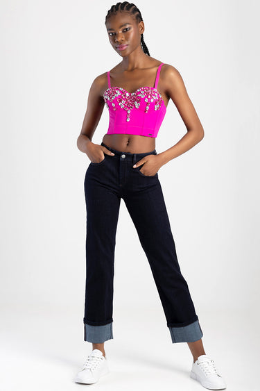 woman wearing bright pink jeweled crop top with dark cuffed jeans and white sneakers