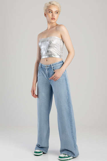 model with short blonde hair wearing a metallic strapless top and light wash wide leg jeans with green and white sneakers