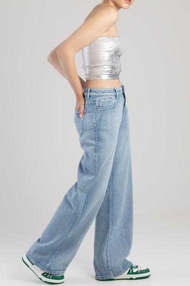 side view of a model in a metallic silver tube top and light blue wide leg jeans with green and white sneakers