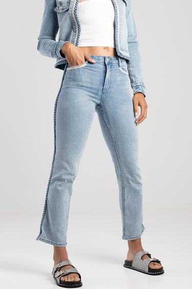 woman wearing light blue straight jeans with a braided side seam, a white crop top, denim jacket, and silver sandals.
