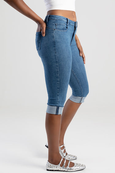side view of a person wearing blue capri jeans with rolled cuffs, a white crop top, and silver studded flats