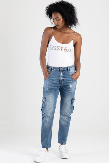 woman in white tank top with rhinestone lettering and blue cargo jeans with distressed knees and white sneakers