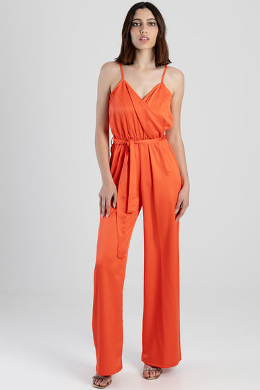 woman wearing an orange wrap front jumpsuit with thin straps and a tied waist belt, wide leg pants.