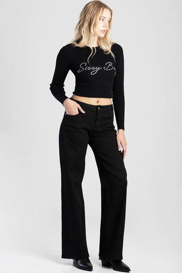 woman in black cropped knit top with silver lettering and black wide leg jeans standing against a light background