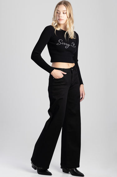 woman wearing a black ribbed cropped top with a script logo and black wide leg jeans with studded ankle boots