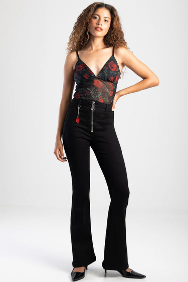 woman standing in black flare jeans with front zipper and heart charm, paired with a sheer black floral top