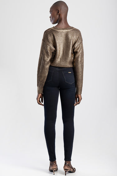 woman in dark skinny jeans with back pockets and a metallic gold knit sweater, shown from behind