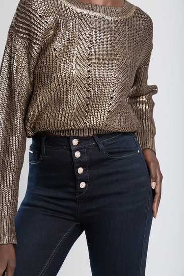 woman wearing dark indigo skinny jeans with five gold buttons and a metallic brown knit sweater