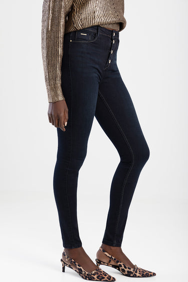woman in dark blue skinny jeans with a button fly, gold metallic knit sweater, and leopard print heeled mary janes.
