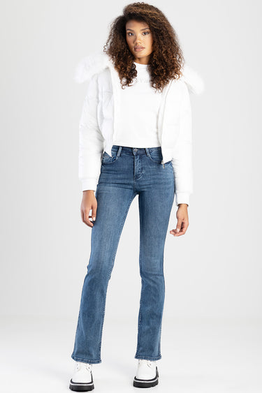 woman in white puffer jacket with fur trim over a white top and blue bootcut jeans paired with white shoes