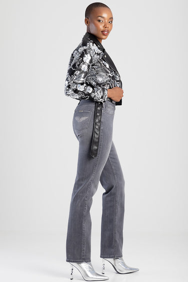 side view of a woman wearing grey straight jeans with a black belt detail, a black and white floral jacket, and silver