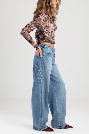woman wearing wide leg blue jeans with a large side cargo pocket and a patterned long sleeve top