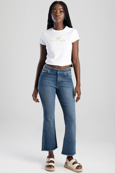 woman wearing Blue Jean Traders flare jeans with a frayed hem, white cropped t shirt, and beige sandals