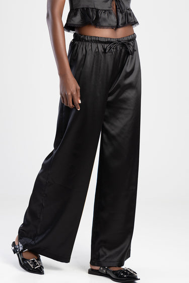 woman wearing black satin wide leg trousers with drawstring waist and elastic waistband, paired with black flats
