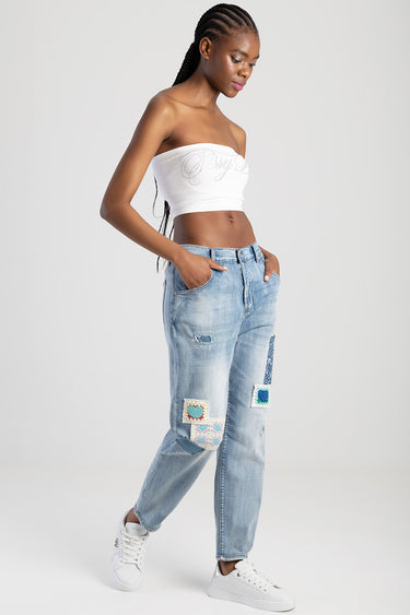 woman in light wash distressed jeans with colorful patches and patchwork, white strapless top and white sneakers