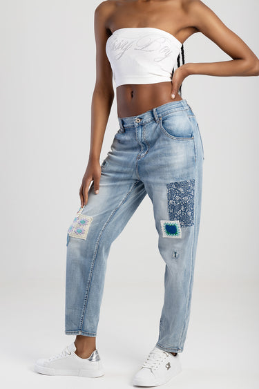 woman wearing light wash straight jeans with patchwork panels on the legs, a white bandeau top, and white sneakers