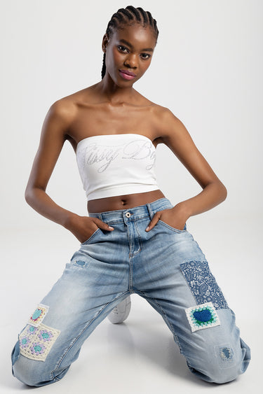 woman in light blue patchwork jeans and white tube top kneeling against a white background
