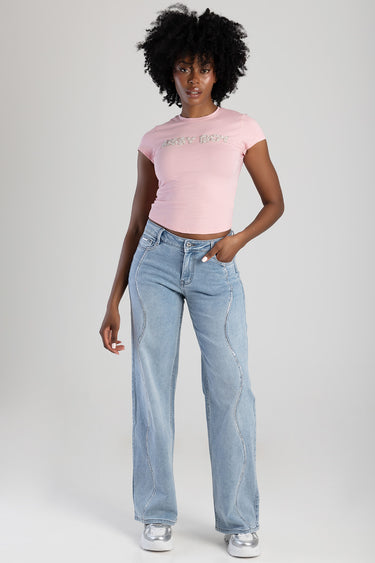 model wearing a pink cropped t shirt with rhinestone logo and light wash wide leg jeans with curved white stitching