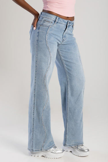 woman in light wash wide leg jeans with rhinestone trim along the outer seam, pink cropped top and white chunky sneakers