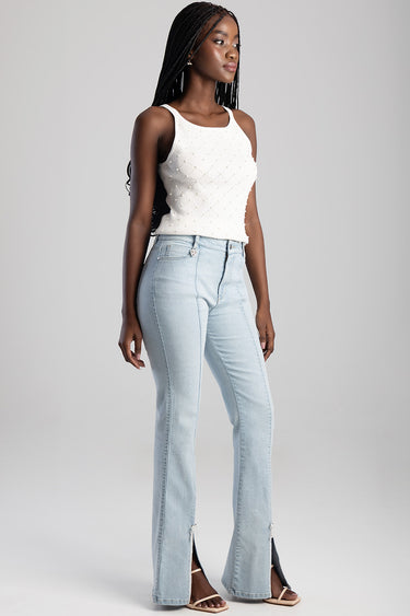 model wearing light wash bootleg jeans with high rise and front pockets, paired with a white knit sleeveless top.