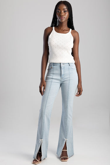 woman in light wash bootcut jeans with front pockets and lace trimmed slits at the hems, paired with a white knit tank top