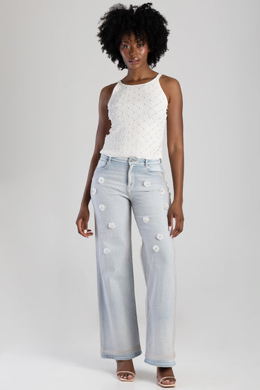 model wearing a white sleeveless textured knit top and light blue wide leg jeans with scattered distressed patches