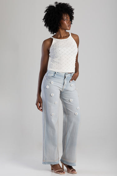 woman in white crochet sleeveless top and light wash wide leg jeans with floral patches