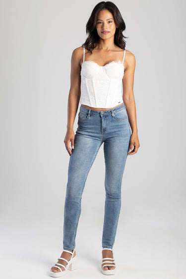 full body shot of a woman in light blue skinny jeans and a white lace corset top with white sandals
