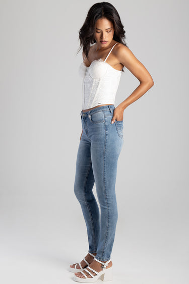 woman in light wash skinny jeans and white lace corset top, standing sideways in white sandals