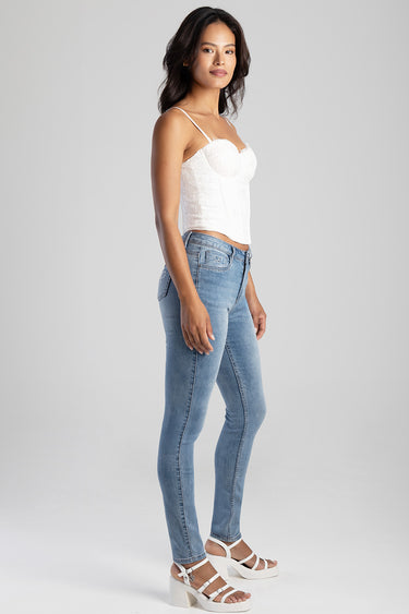 woman wearing light blue skinny jeans with a white lace top and white sandals in a studio.