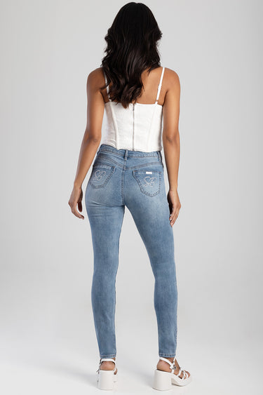 woman wearing light blue skinny jeans with embroidered back pockets and a white lace corset top, back view