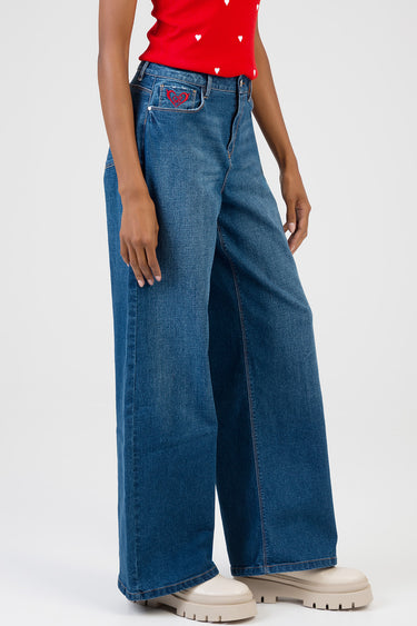 woman wearing blue wide leg jeans with a red heart embroidery on the front pocket