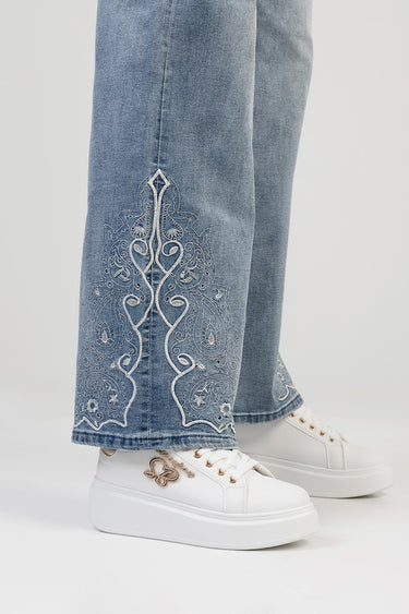 blue denim jeans with white ornate embroidery at the lower leg, paired with white platform sneakers and gold eyelet details