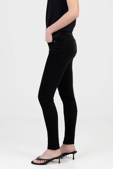woman in black skinny pants and black top, side view, hands in pockets, wearing black heeled sandals.