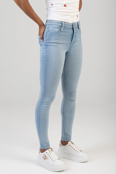 model wearing light blue skinny jeans and white sneakers, standing with hands in pockets